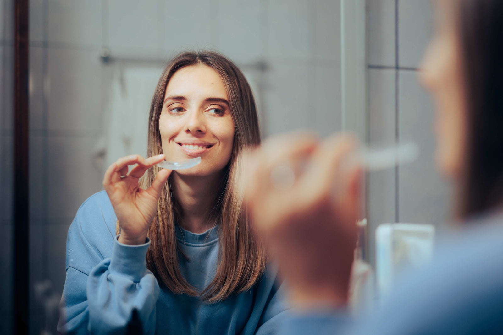 smiling woman in bathroom mirror putting on night guard